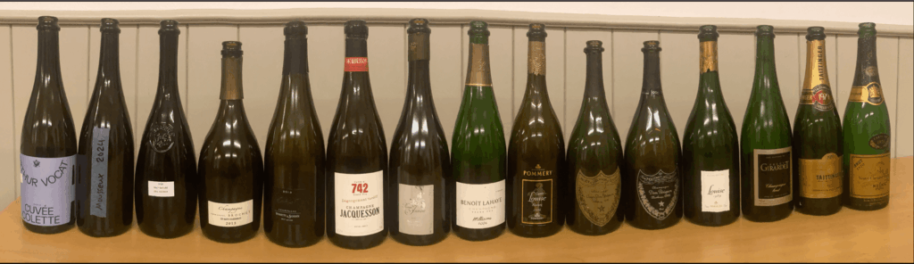 Une sélection de champagnes millésimés et prestige, de 2015 à 1970, incluant des cuvées de Jacquesson, Dom Pérignon, Veuve Clicquot et Taittinger, alignées sur un comptoir en bois, avec étiquettes variées et bouchons dorés ou argentés, dans un cadre lumineux et épuré.