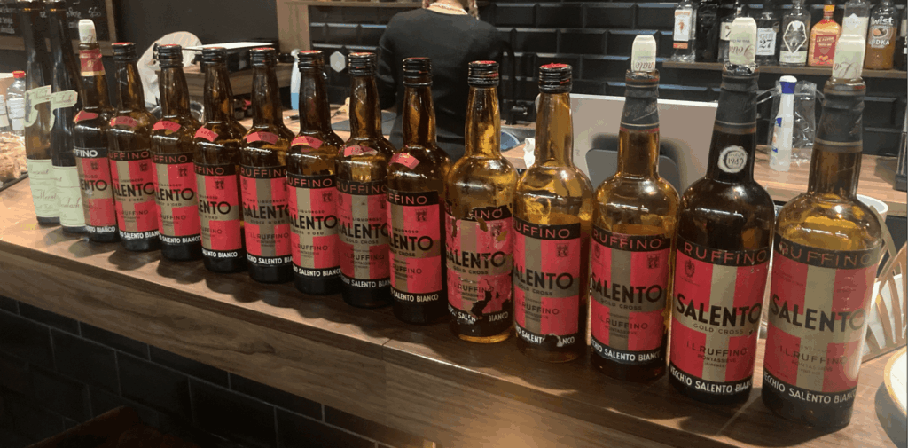Une série de bouteilles de Ruffino Vecchio Salento Bianco, millésimes 1937 à 1973, alignées sur un comptoir en bois, présentées lors d’une dégustation à Sion