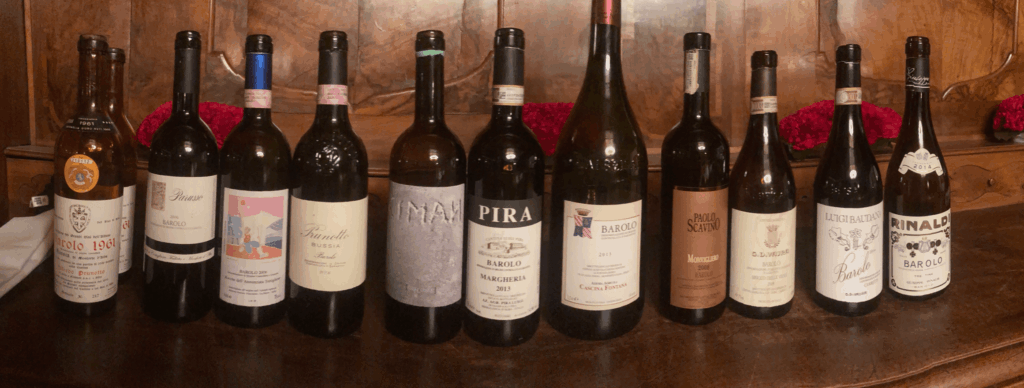 Une sélection de dix bouteilles de Barolo de grands crus italiens, alignées sur un meuble en bois sombre, dont les étiquettes incluent Prunotto, Pira, Scavino, Rinaldi et autres domaines emblématiques du Piémont.