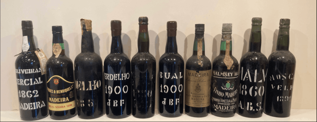 Une sélection de bouteilles de Madère du XIXe siècle, dont certaines datant de 1860 à 1900, présentées lors d’une dégustation historique organisée par Wine Rose en Suisse romande, mettant en valeur des vins rares et vieillis en fût ou en dame-jeanne.