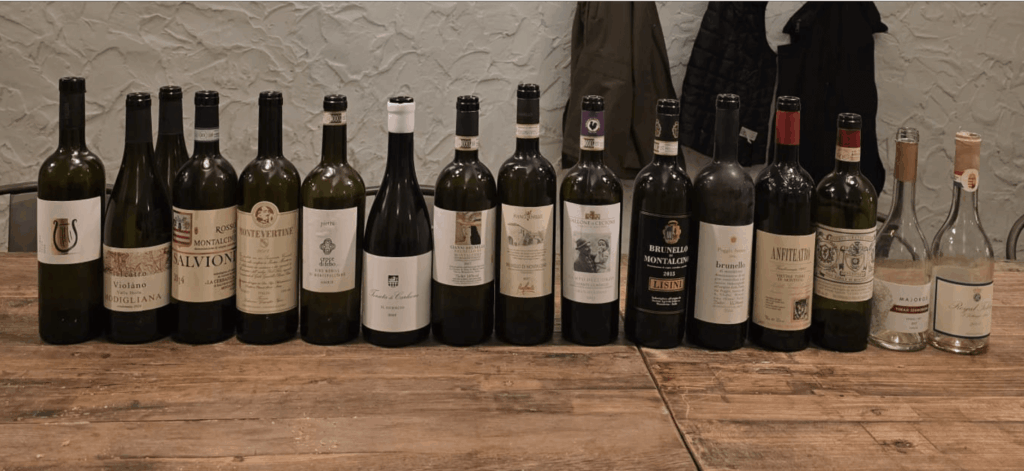 Une sélection de douze bouteilles de vins italiens à base de Sangiovese, alignées sur une table en bois, incluant des Brunello, Rosso di Montalcino et Chianti, présentées lors d’une dégustation à Zurich.