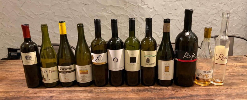 Une sélection de onze bouteilles de vins d'orange et blancs du Frioul et de Slovénie, présentées sur une table en bois pour une dégustation de collectionneurs.