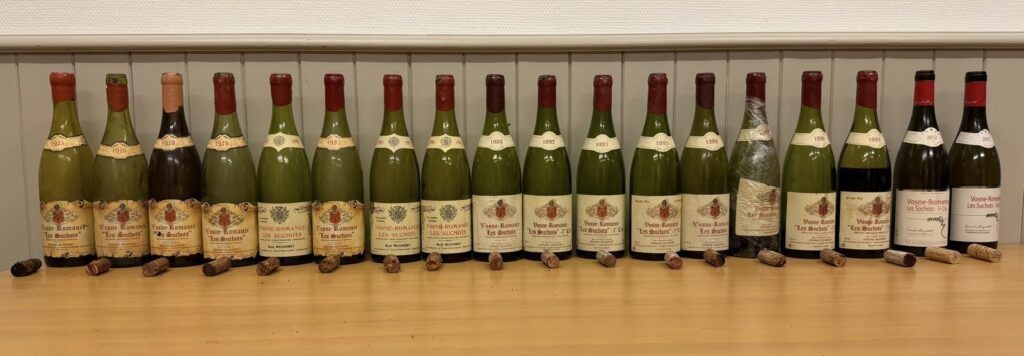Ligne de 17 bouteilles de Vosne-Romanée Les Suchots du domaine Gérard Mugneret, couvrant les millésimes de 1975 à 2017, présentées avec leurs bouchons pour une dégustation verticale à Saint-Saphorin.